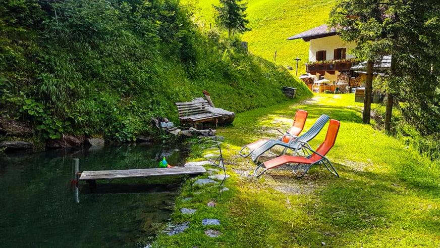 Gartenanlage vom Alpengasthof Bad Kalkstein Innervillgraten mit Teich, Liegestühlen und Rasenfläche.