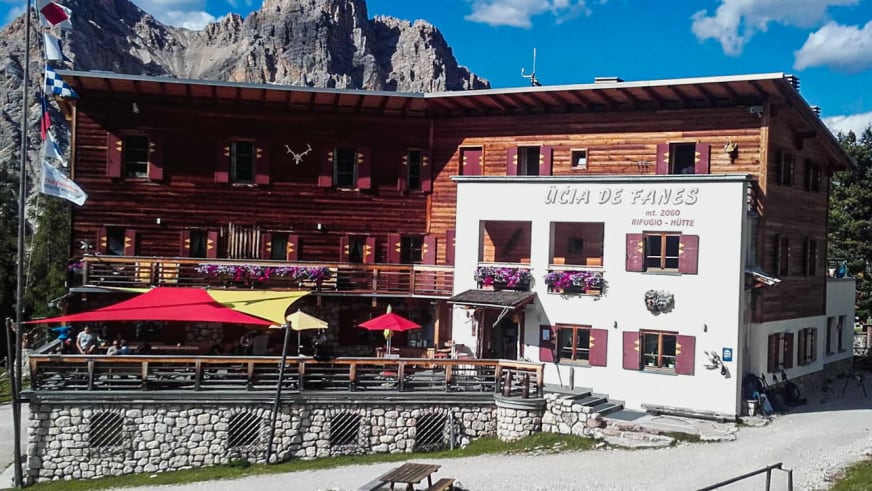Die Faneshütte auf 2060 m zeigt traditionelle Alpenarchitektur mit Holzverkleidung, roten Fensterläden und violetten Blumenkästen vor steilen Felswänden.