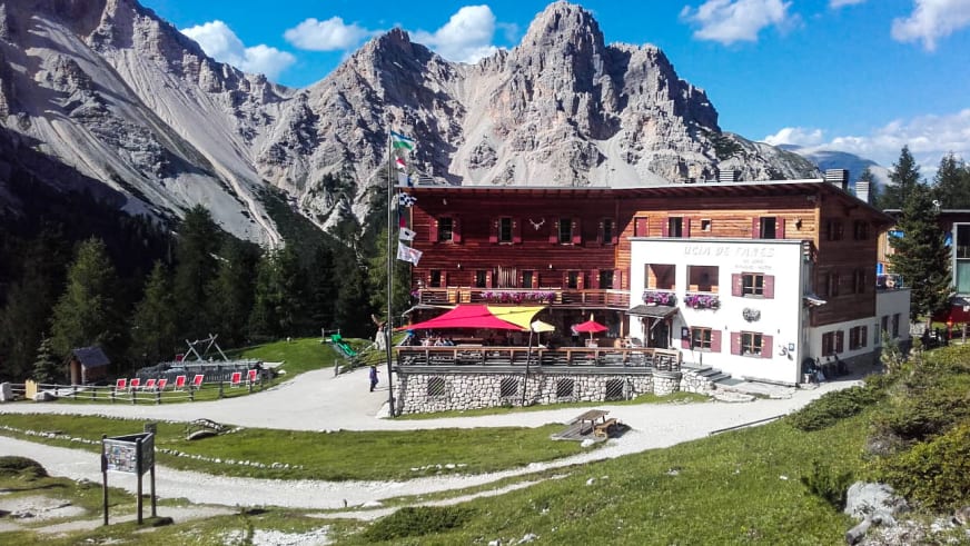 Sommeraufnahme der Faneshütte (Rifugio Fanes) auf grüner Almwiese vor steiler Dolomitenfelsband.