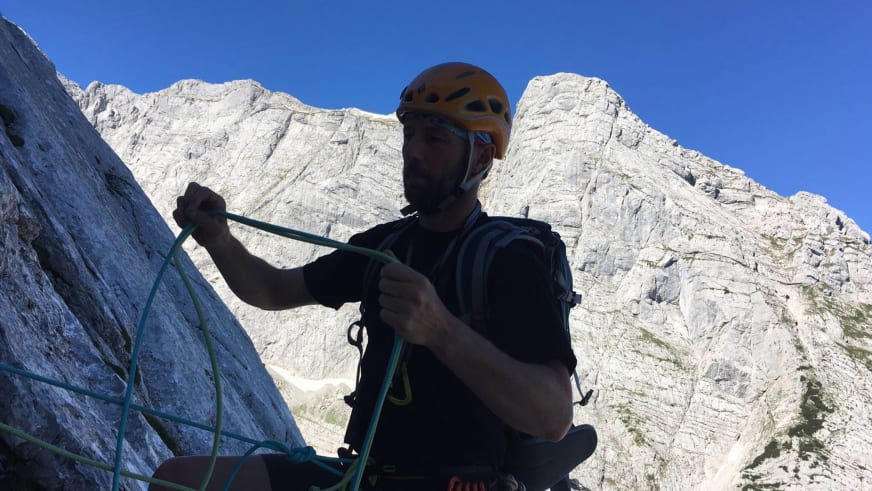 Skilehrer Jürgen Brandhuber hält grünes Kletterseil vor grauer Kalksteinwand mit orangem Helm und Klettergurt.