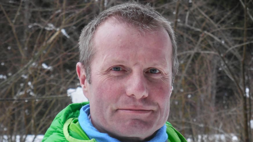 Bergwanderführer Albert Bucher trägt grüne Softshell-Jacke über blauem Fleece vor verschneitem Hintergrund.