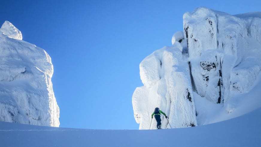 Bergführer Sebastian Conrad fährt mit Tourenskiern durch pulvrigen Tiefschnee zwischen weiß verhangenen Felsformationen.