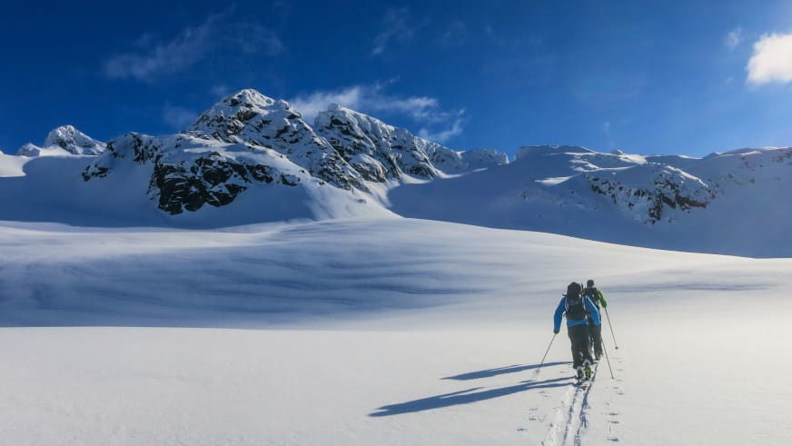 Zwei Skitourengeher bewegen sich durch unberührten Tiefschnee, geführt von Bergführer Sebastian Conrad in blauer Jacke.