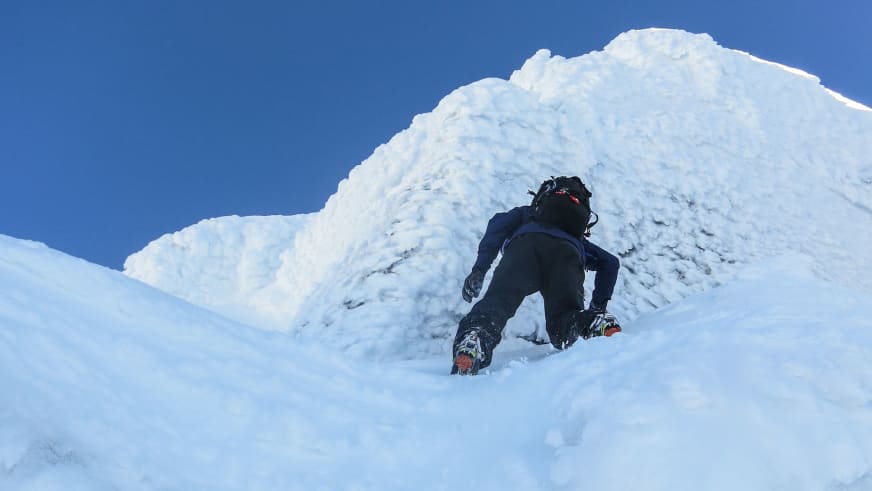 Eine Person in dunkler Winterkleidung steigt einen steilen verschneiten Hang hinauf, Bergführer Sebastian Conrad auf Hochtour.