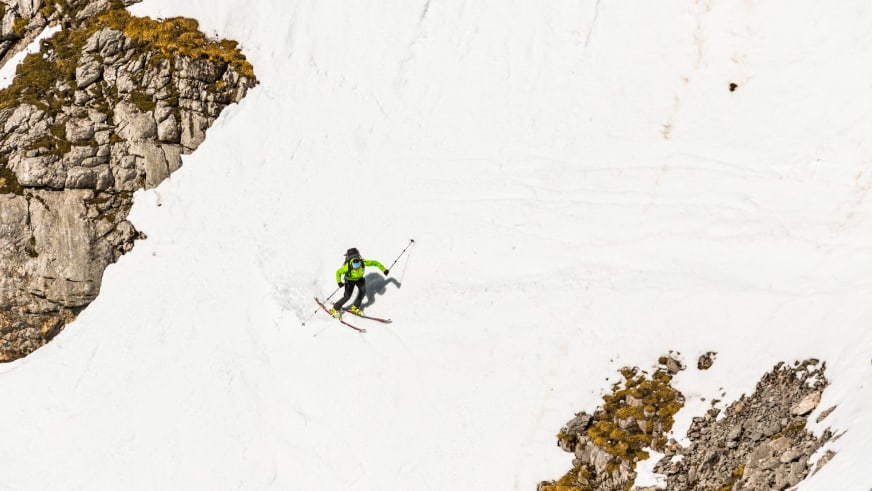 In neongrüner Jacke und weißem Helm fährt Skilehrer Benedikt Fritz eine steile Schneeflanke zwischen Felswänden hinab.