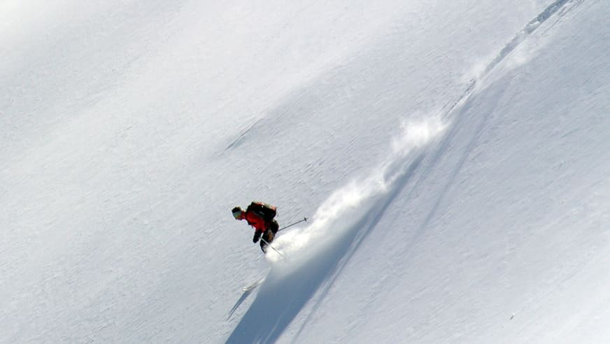 Durch unverspurten Tiefschnee fährt Bergführer Walter Hölzler in roter Jacke einen steilen Hang hinab.
