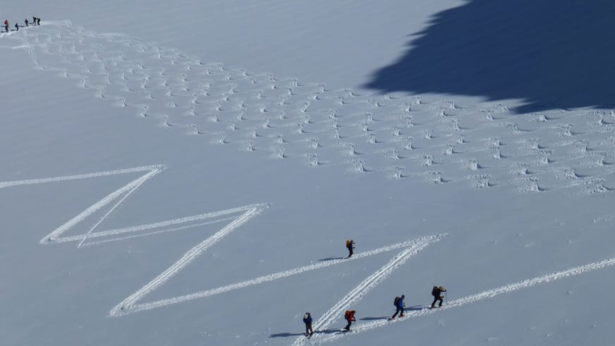 Eine Gruppe von fünf Skitourengehern bewegt sich mit Bergführer Walter Hölzler diagonal durch den Tiefschnee am Piz Buin.
