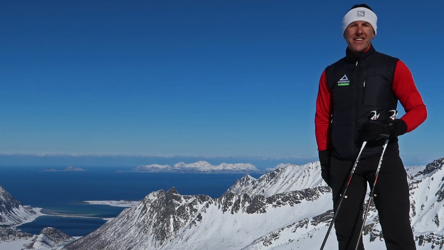 Auf einem schneebedeckten Hang steht Bergführer Walter Hölzler mit Skistöcken vor einer weiten Gebirgslandschaft.