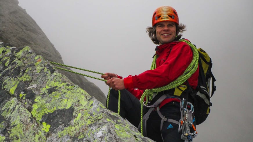 Bergführer Michael Hornsteiner seilt sich in roter Jacke und orangem Helm mit grünem Kletterseil an einer Felswand ab.