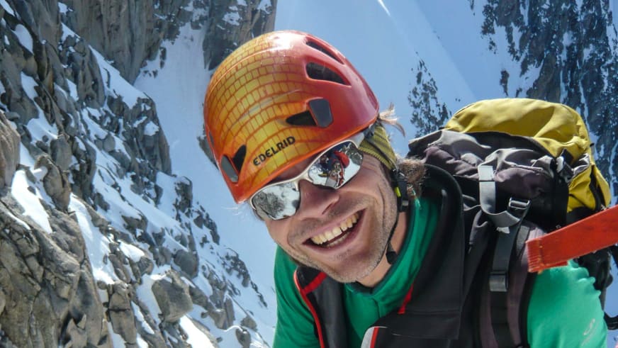 Bergführer Michael Hornsteiner mit Gletscherbrille und orangem Helm vor schneebedeckter Felswand am Mont Blanc.
