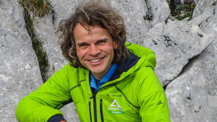 Bergführer Michael Hornsteiner in grüner Vaude-Jacke lächelt vor einer strukturierten Felswand aus hellem Kalkstein.