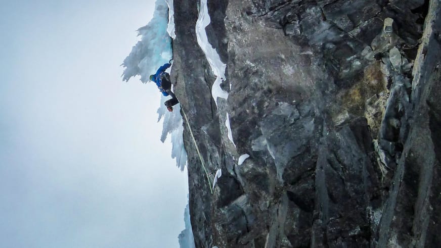 Bergführer Christoph Hummel klettert in blauer Winterkleidung mit Eisgeräten an einer vereisten Felswand in Norwegen.