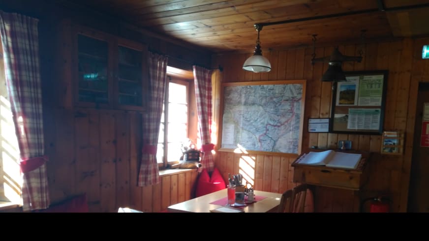 Gemütlicher Gastraum der Siegerlandhütte mit Holzbalkendecke und traditioneller Bergkarten-Ausstattung.