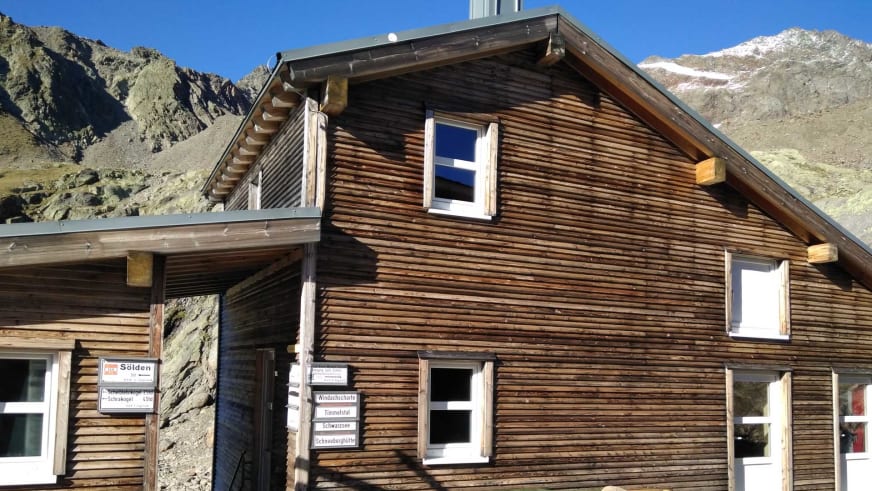 Fassade der Siegerlandhütte mit verschiedenen Wegweiser-Schildern und Richtungsangaben zu alpinen Zielen.