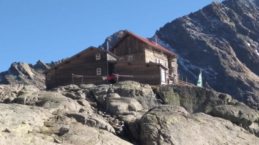 Die Siegerlandhütte steht auf hellem Kalkfelsplateau mit Holz-Stein-Bauweise vor steilen Felswänden.
