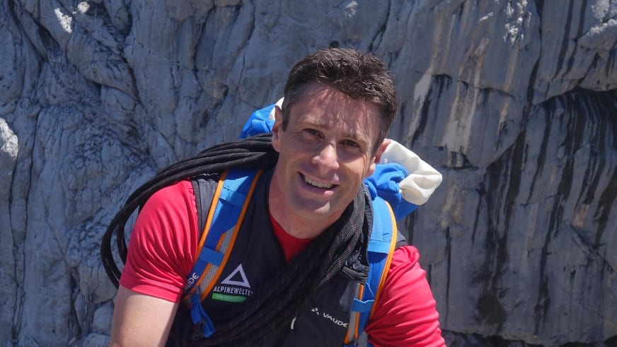 Portrait von Bergführer Simon Kraus mit rotem Funktionsshirt und Kletterseil vor grau-bläulicher Felswand an der Zugspitze.