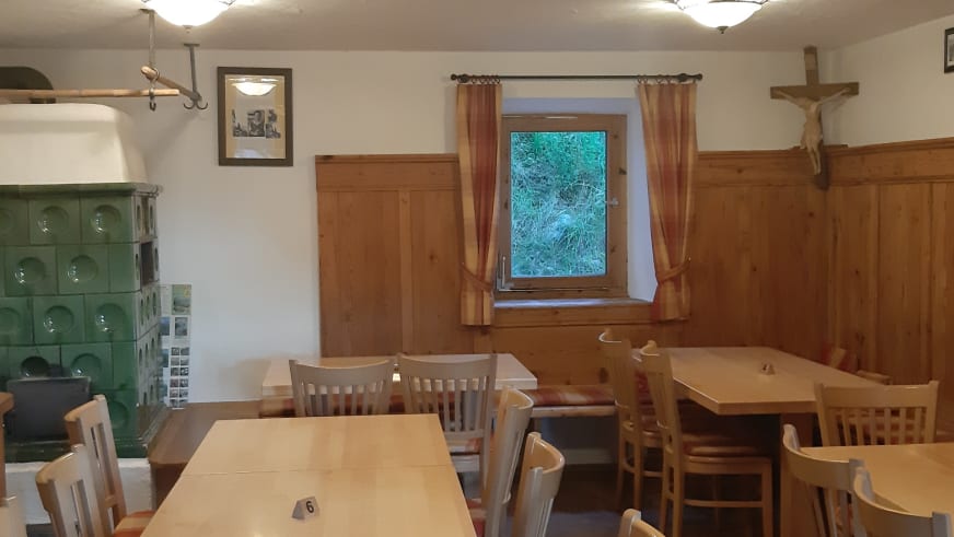 Innenraum der Gaudeamushütte mit nummerierten Holztischen und grünem Kachelofen zur Beheizung.