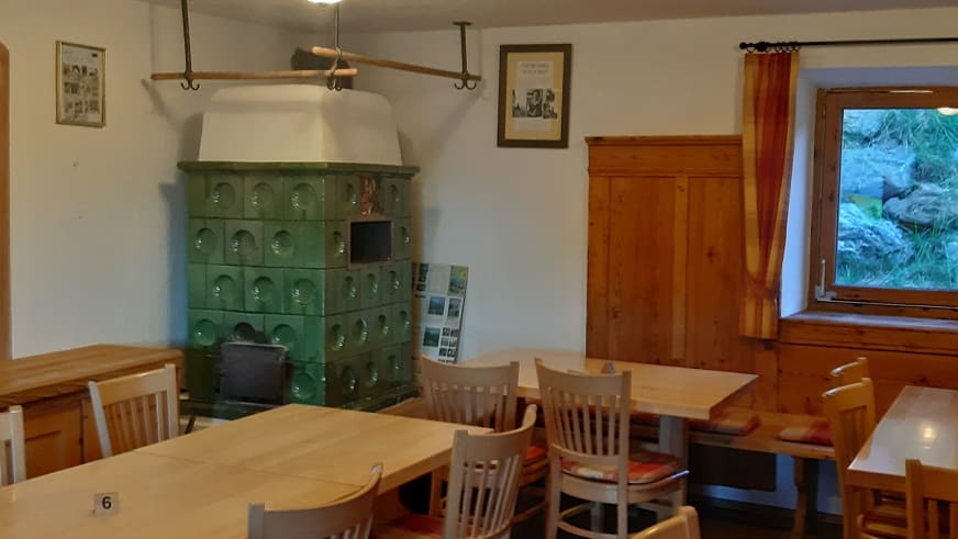 Gemütliche Gaststube in der Gaudeamushütte mit grünem Kachelofen und traditionellen Holztischen.