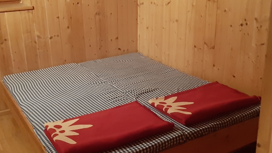 Schlafzimmer der Gaudeamushütte mit Doppelbett und blau-weiß karierter Bettwäsche aus Holz.