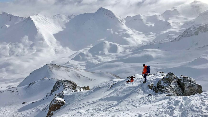 Bergführer Simon Kraus steht mit zweiter Person auf schneebedecktem Gipfelgrat zwischen Felsformationen in den Ostalpen.
