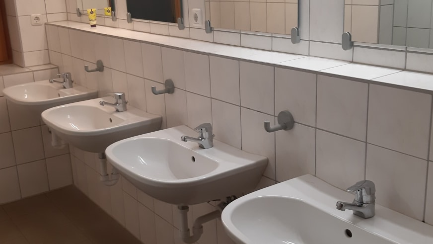 Moderner Waschraum der Gaudeamushütte mit vier weißen Waschbecken und gefliesten Wänden.