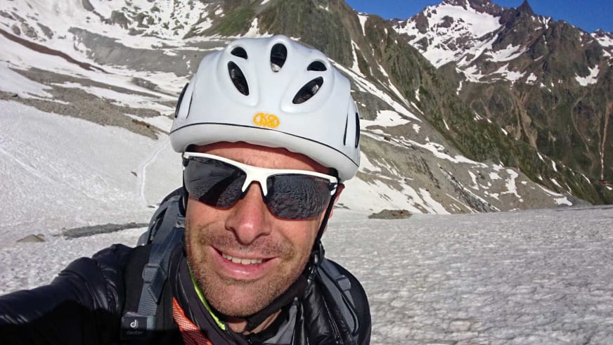 Selbstporträt von Bergführer Simon Kraus mit weißem Helm und Sonnenbrille in schneebedeckter Gletscherlandschaft.