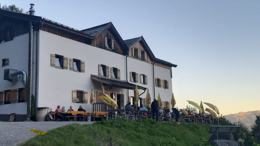Bergsteiger vor der Gaudeamushütte auf der Terrasse mit orangefarbenen Bierbänken im Kaisergebirge.