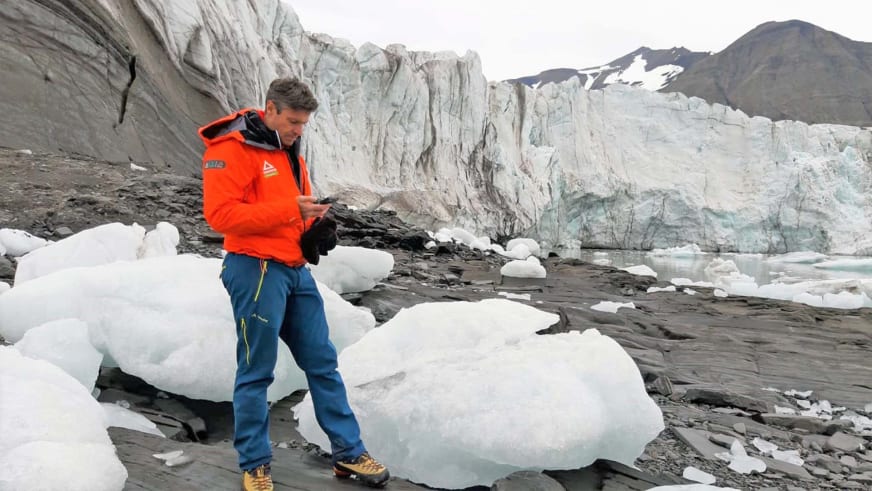 Bergführer Simon Kraus steht in orangefarbener Jacke zwischen weißen Eisblöcken vor einer großen Gletscherwand.