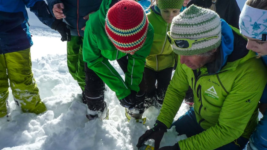 Bei einem Lawinenkurs kniet Bergführer Martin Bauregger im Schnee und erklärt fünf Teilnehmern die Schneeschicht.