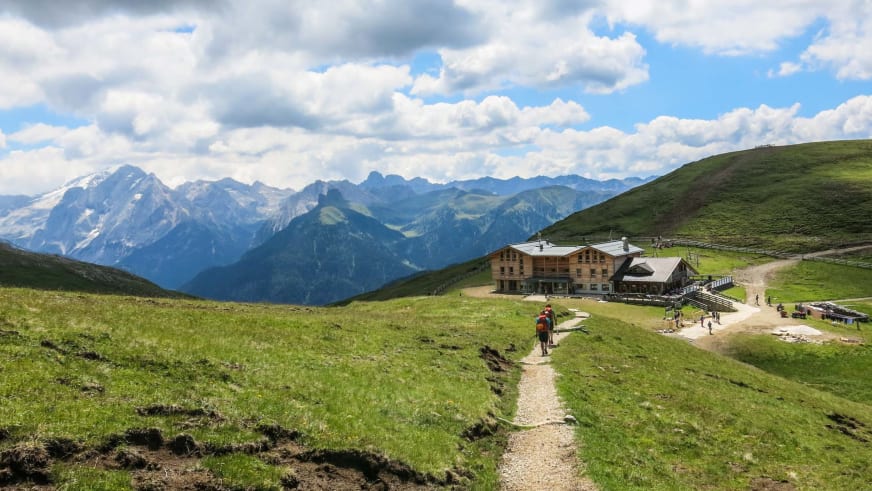 Zwei Wanderer mit Rucksäcken gehen auf Schotterweg zur Plattkofelhütte auf grünem Hochplateau.