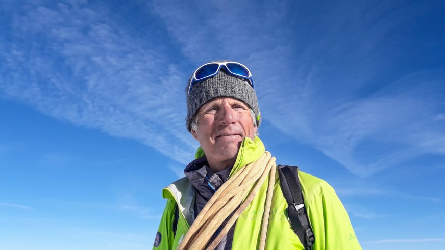 Bergführer Martin Bauregger trägt neongrüne Hardshelljacke und Seil über der Schulter vor strahlend blauem Himmel.