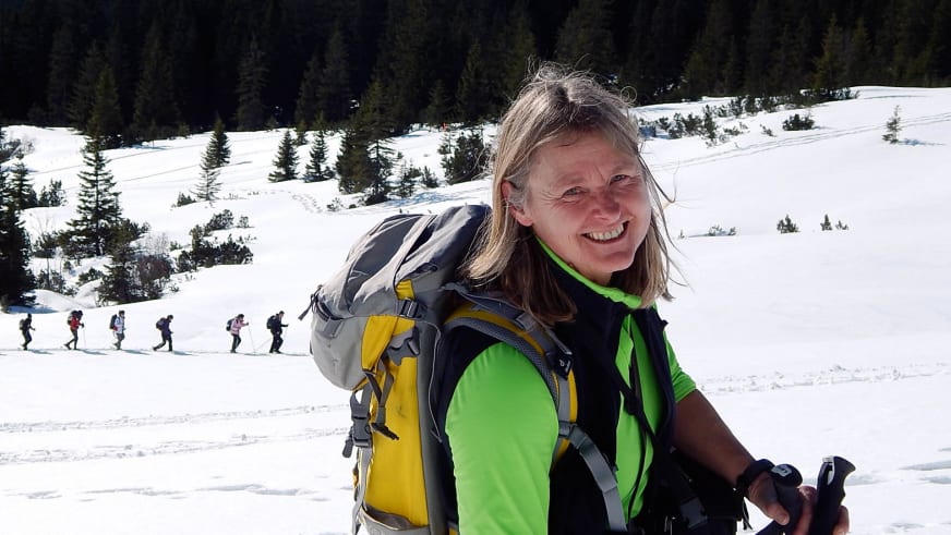 Bergwanderführerin Isolde Fink mit grüner Jacke und schwarzen Wanderstöcken führt eine Gruppe durch verschneite Berglandschaft.