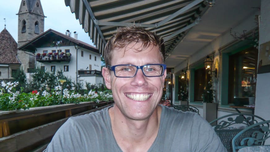 Bergführer Jens Lang sitzt entspannt auf einer überdachten Terrasse vor Alpenarchitektur mit weißem Haus.