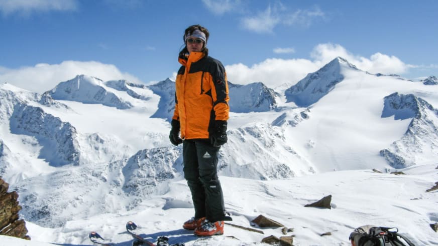 Auf verschneitem Gipfelplateau steht Bergwanderführerin Angelika Neubauer auf Skiern vor schneebedeckten Bergen.