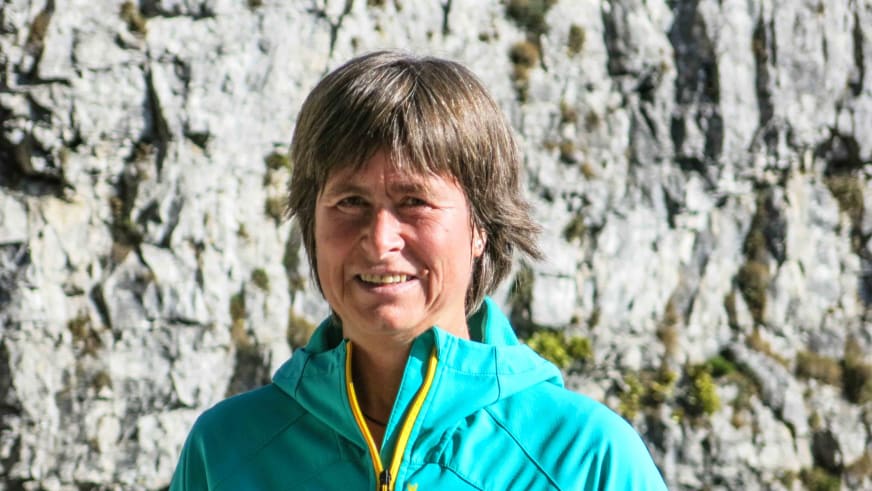 Portrait von Bergwanderführerin Angelika Neubauer mit türkiser Jacke vor einer strukturierten Kalksteinwand bei Tageslicht.