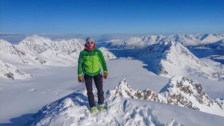 Bergführer Jörg Rauschenberger steht auf dem verschneiten Tafeltinden vor weitläufiger Fjordlandschaft in den Lyngen Alpen.