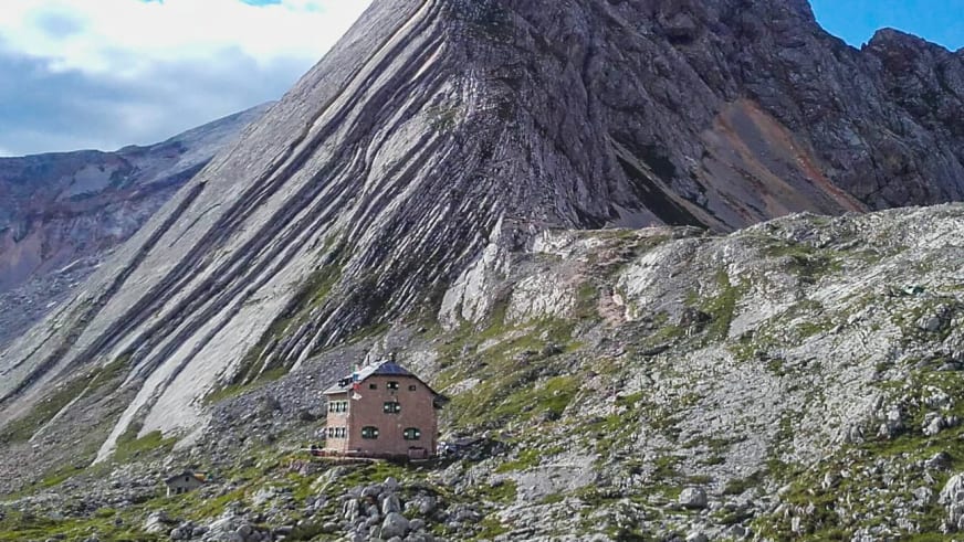 Die Seekofelhütte steht auf einem Geröllplateau zwischen Felsblöcken mit steilen Felshängen im Hintergrund der Dolomiten.