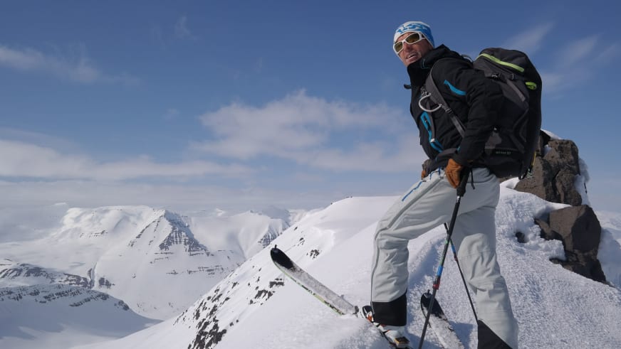 Auf verschneitem Felsvorsprung steht Bergführer Jörg Rauschenberger mit blauer Mütze und schwarzer Softshell-Jacke.