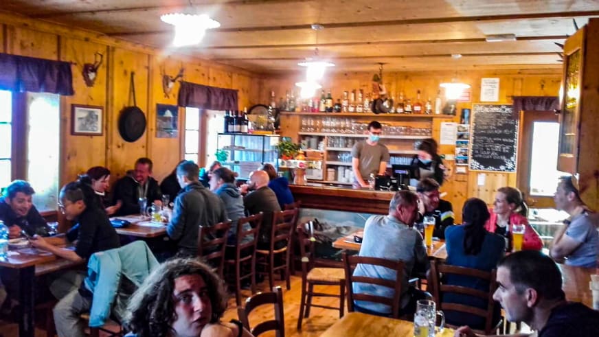 Innenraum der Seekofelhütte (Rifugio Biella) mit rustikaler Holzeinrichtung und Gästen an Holztischen im Gastraum.