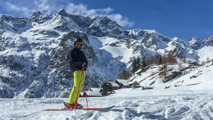 Bergwanderführer Karlheinz Rösch auf Skiern in verschneiter Landschaft mit Bergdorf und Gipfeln im Hintergrund.