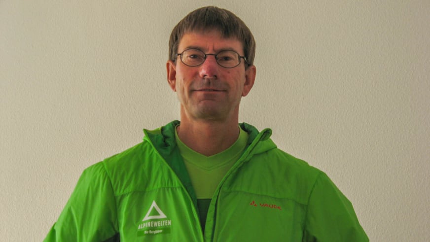 Bergwanderführer Karlheinz Rösch trägt grüne Vaude-Jacke mit Alpine Welten Logo und lächelt in die Kamera.
