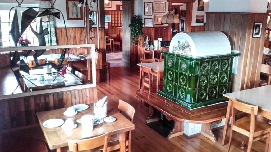 Rustikaler Gastraum im Rifugio Cinque Torri mit Holztischen, grünem Kachelofen und traditioneller Alpenhütten-Ausstattun