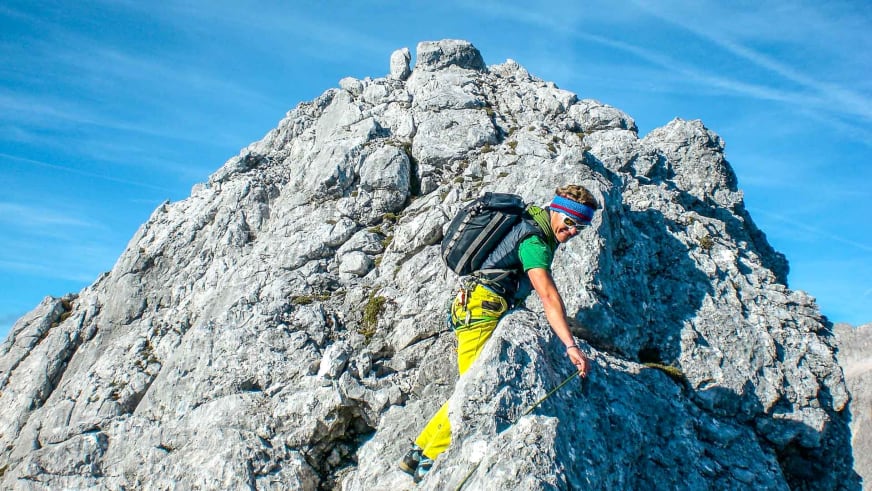 Bergführer Marcel Roßbach in gelber Kletterhose greift an einer steilen Kalksteinwand nach einem Felsgriff.