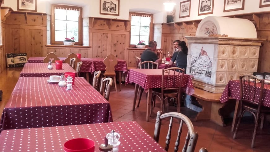Traditionelle Gaststube im Rifugio Croda da Lago mit Holzvertäfelung, gedeckten Tischen und weißem Kachelofen.