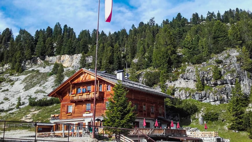 Außenansicht der Dürrensteinhütte mit rot-weiß-roter Fahne vor steiler Kalksteinwand der Dolomiten.