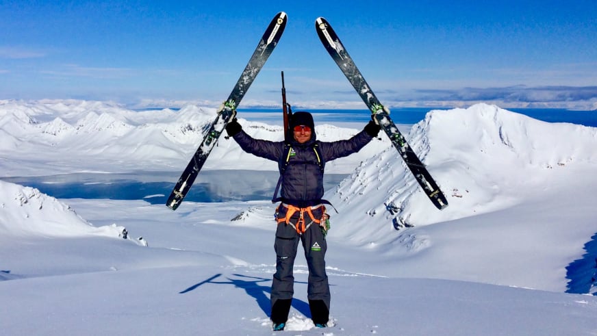 Bergführer Marcel Roßbach hält seine Skier triumphierend über den Kopf auf einem verschneiten Gipfel.