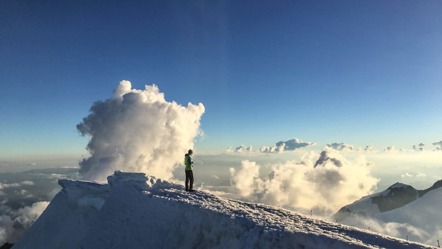 Bergführer Michael Rüter steht in grüner Jacke auf einem verschneiten Gipfelgrat oberhalb der Wolken.