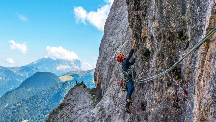 Bergführer Michael Rüter klettert mit orangem Helm an einer steilen Felswand entlang eines Drahtseils.