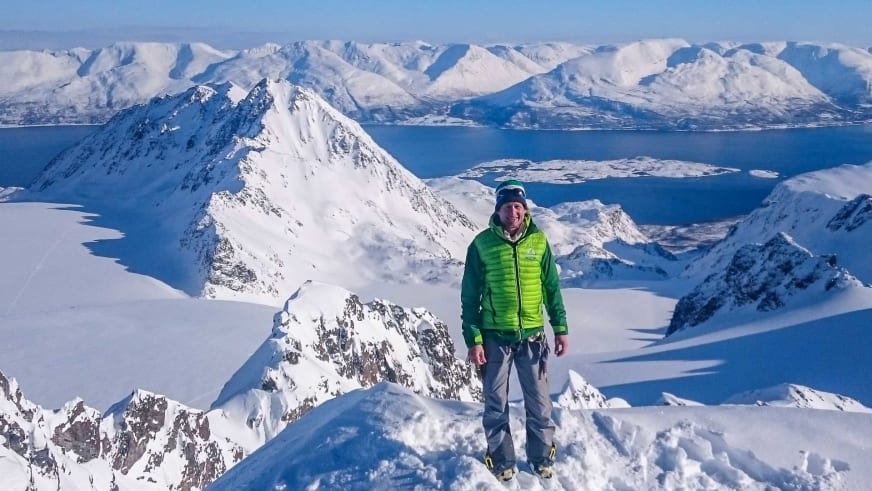 Auf einem verschneiten Gipfel in Norwegen steht Bergführer Michael Rüter mit Blick über die Fjordlandschaft.