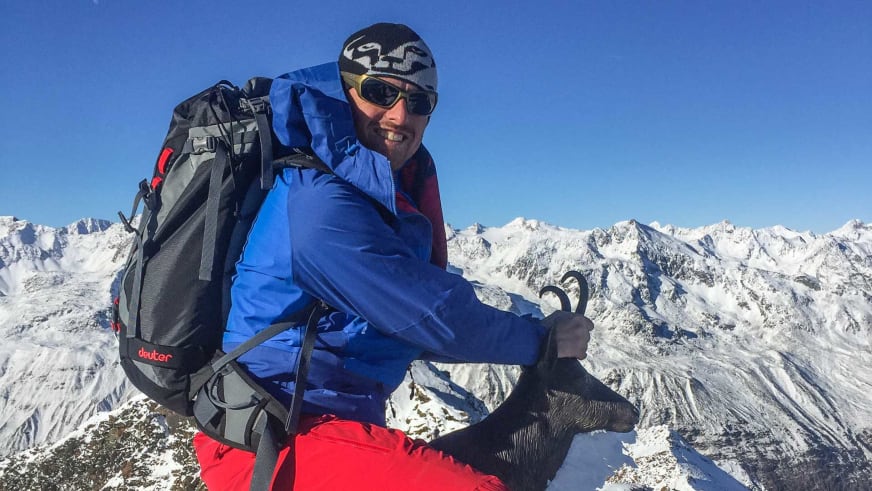 Bergführer Florian Schmidt steht mit Skistöcken auf einem verschneiten Gipfel in der Silvretta und lächelt in die Kamera.